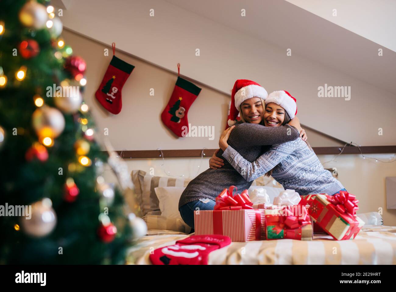 Deux belles filles célébrant la nouvelle année ensemble. Assis sur le lit avec bouquet de cadeaux devant eux. Banque D'Images