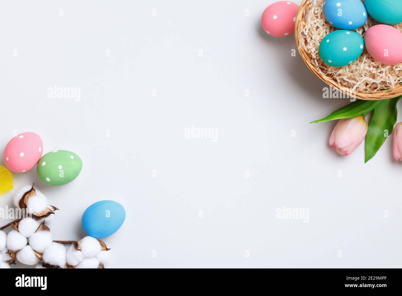 Joyeuses Pâques. Oeufs multicolores dans un panier, tulipes et branche de coton sur fond gris. Espace de copie de carte de vœux à plat. Banque D'Images