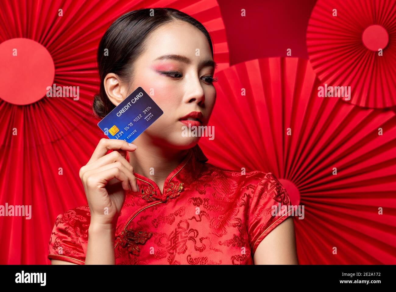 Gros plan de la belle femme asiatique portant un cheongsam traditionnel robe qipao montrant la carte de crédit à la main sur rouge oriental Contexte pour les Chines Banque D'Images