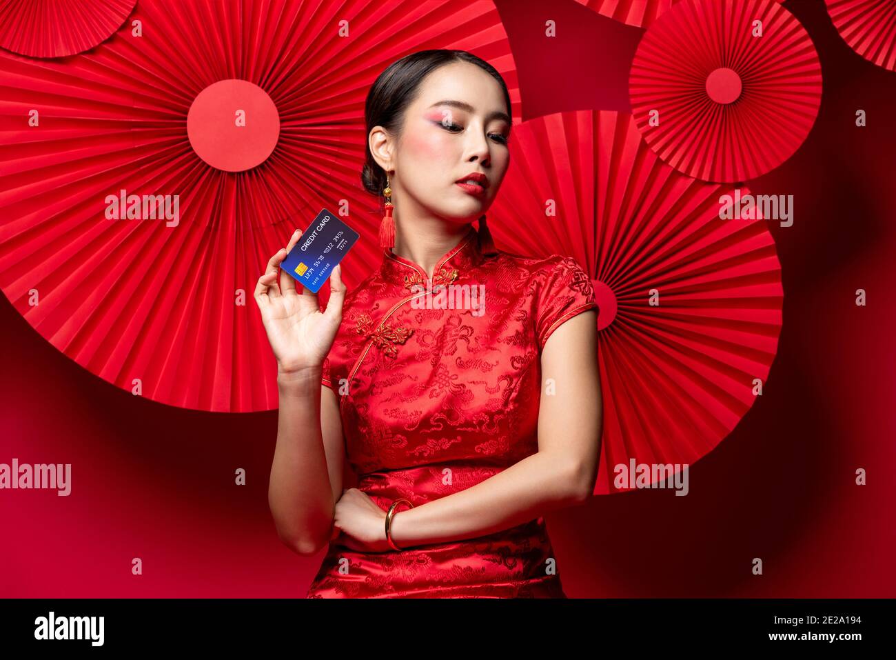 Belle femme asiatique portant la robe traditionnelle de cheongsam qipao montrant le crédit Carte en main sur fond oriental rouge pour nouveau chinois achats de l'année c Banque D'Images