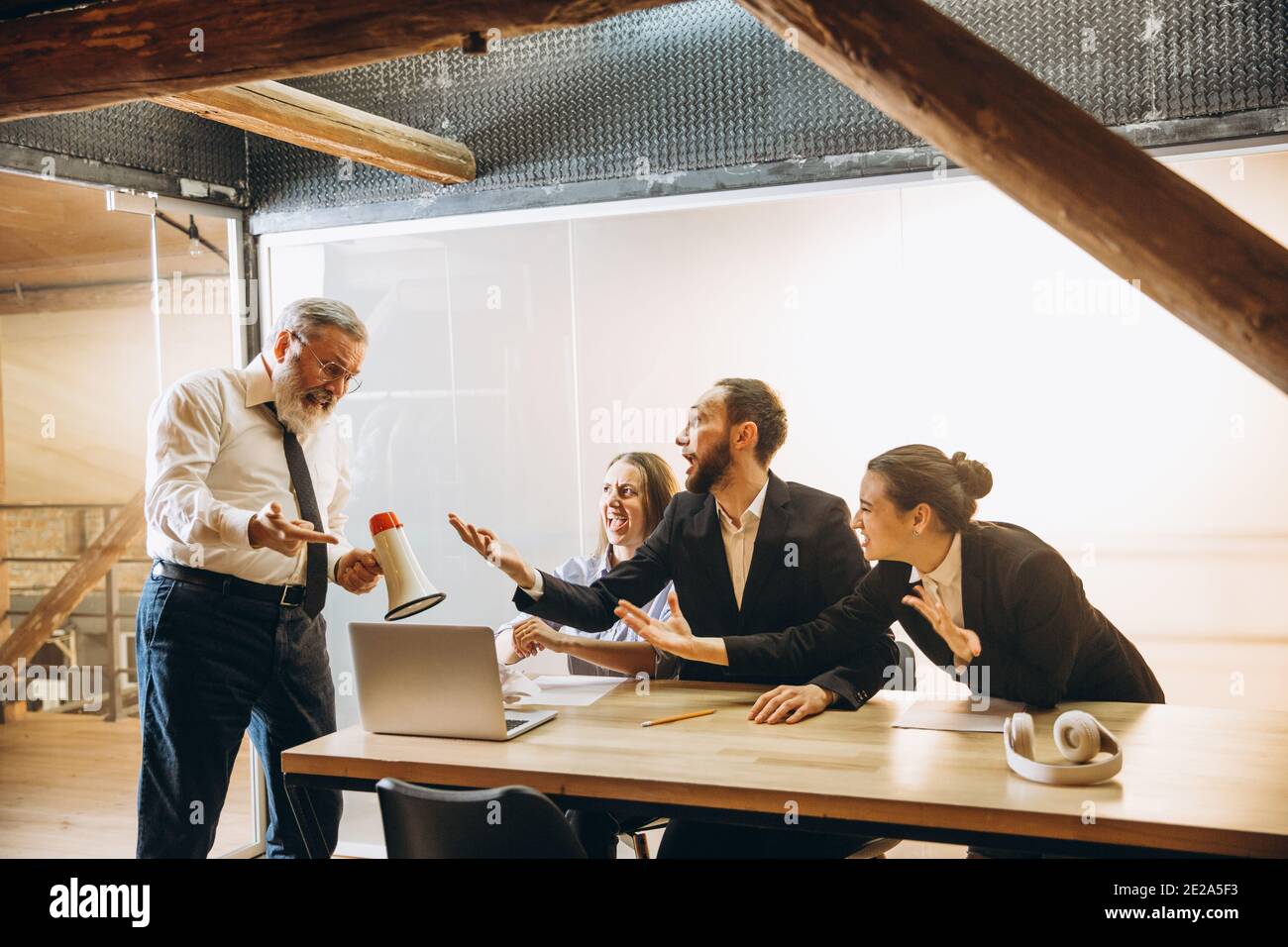 Lutte. Un patron en colère avec un mégaphone hurlant aux employés au bureau, des collègues effrayés et agacés à l'écoute de la table ont été stressés. Concept de réunion, d'affaires, de bureau amusant. Hurler fou. Banque D'Images