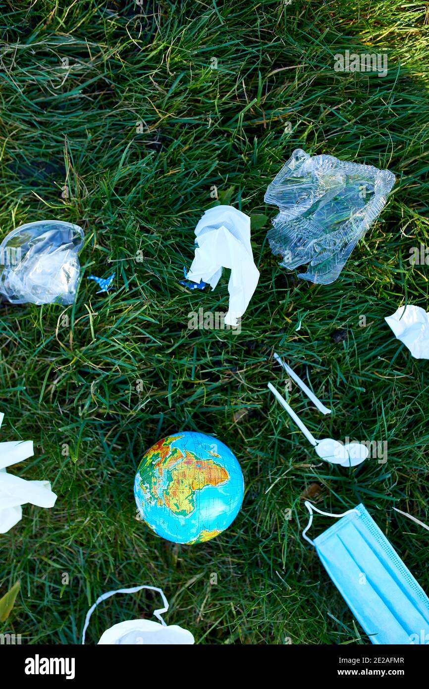 Un globe dans une pile de déchets éparpillés sur un fond d'herbe verte, autour de plastique dispersé, masque de protection, gants, déchets pendant la casserole du coronavirus Banque D'Images