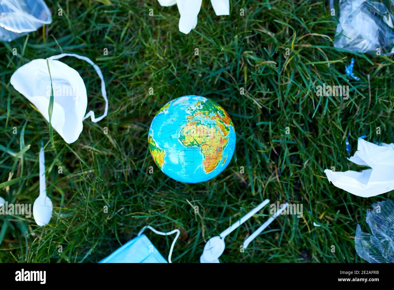 Un globe dans une pile de déchets éparpillés sur un fond d'herbe verte, autour de plastique dispersé, masque de protection, gants, déchets pendant la casserole du coronavirus Banque D'Images