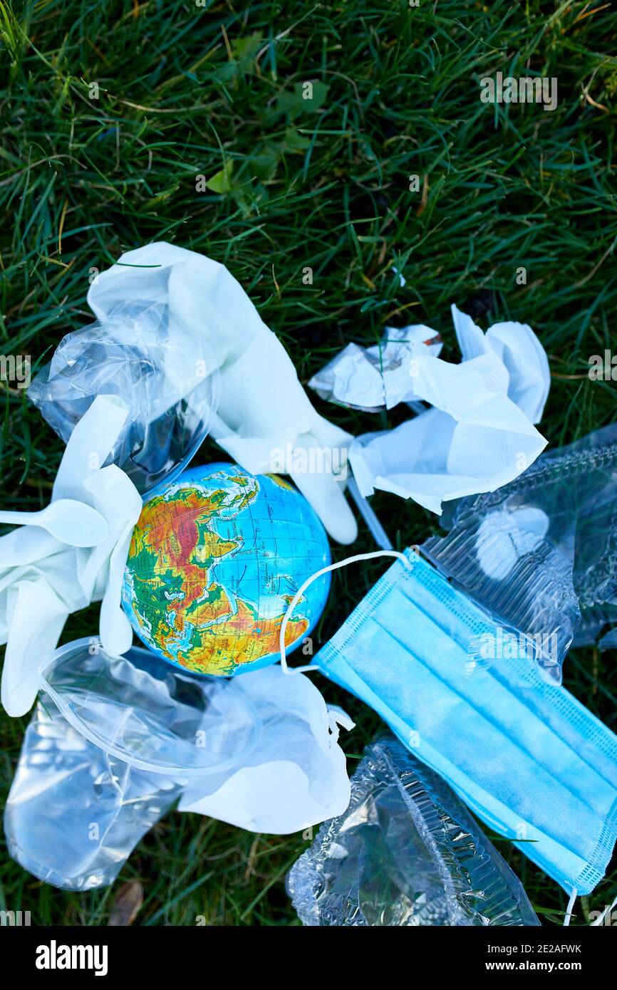 Un globe dans une pile de déchets éparpillés sur un fond d'herbe verte, autour de plastique dispersé, masque de protection, gants, déchets pendant la casserole du coronavirus Banque D'Images