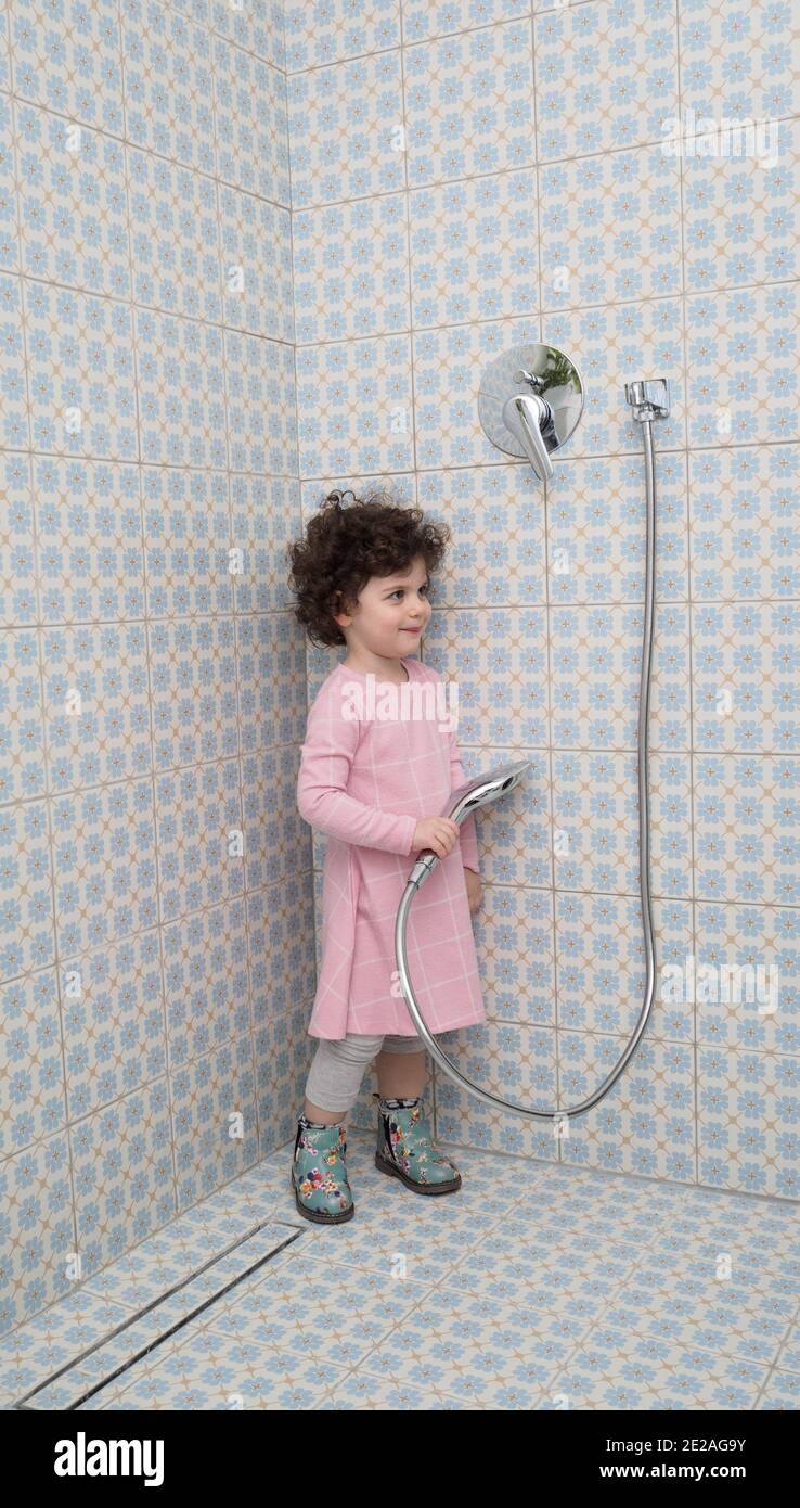 Entièrement habillée, la petite fille joue dans la douche Banque D'Images