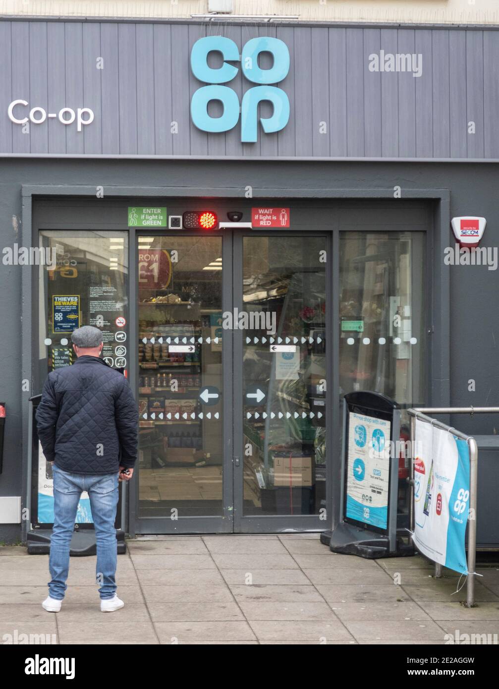 Un homme attend d'entrer dans un système de feux de circulation, Co op supermarché magasin pendant les restrictions Covid coronavirus à Sidmouth Devon Royaume-Uni Banque D'Images
