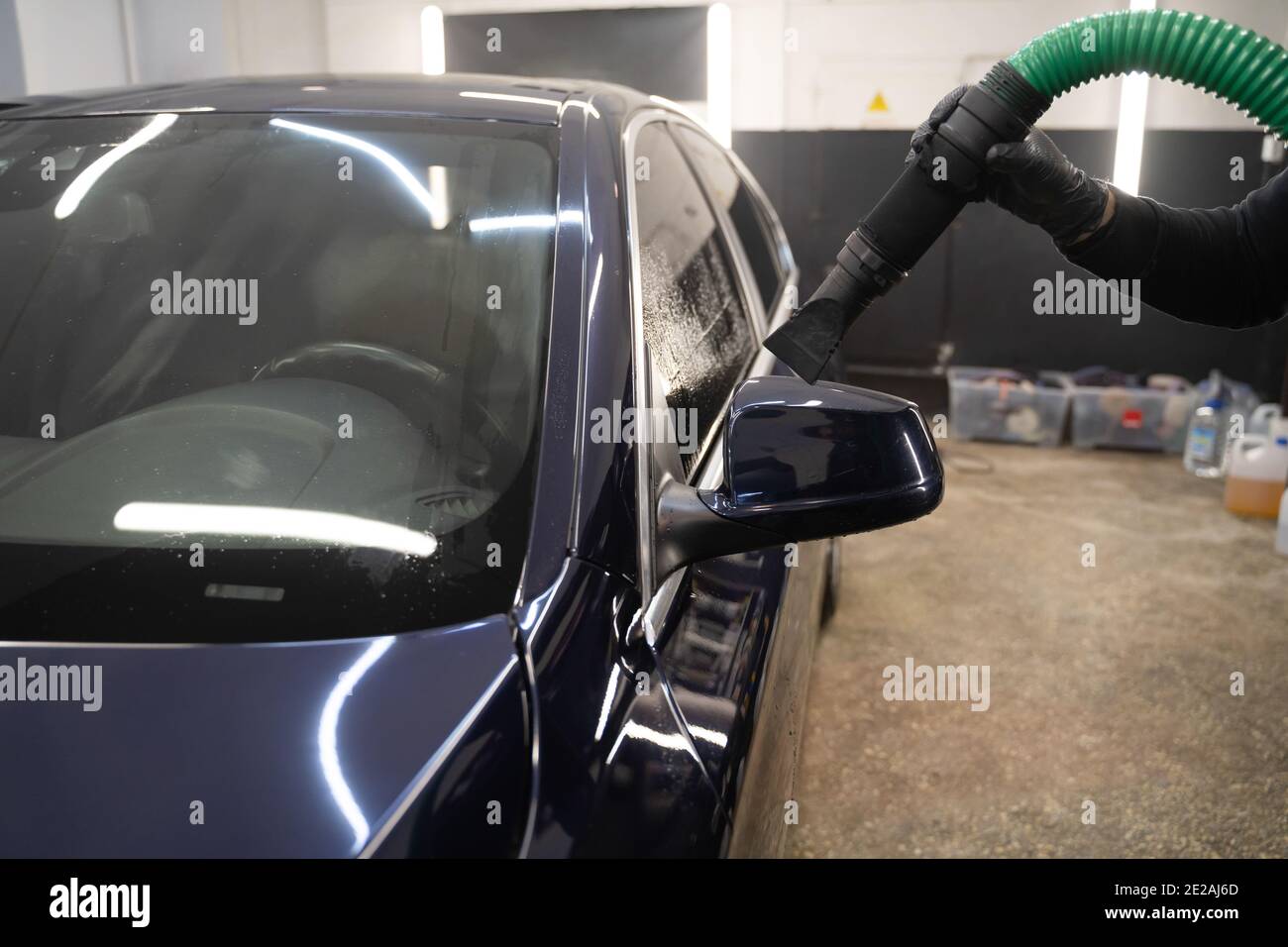 Processus de séchage de voiture après lavage. L'homme équipé d'un aspirateur élimine les gouttelettes d'eau de la voiture. Concept de lavage automatique professionnel Banque D'Images