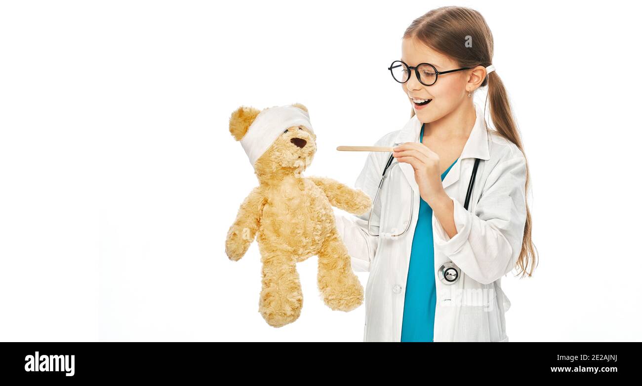 Une fille caucasienne jouant avec son patient ours en peluche dans un jeu de docteur, en utilisant la spatule d'inspection de gorge. L'enfant veut être un médecin ORL Banque D'Images