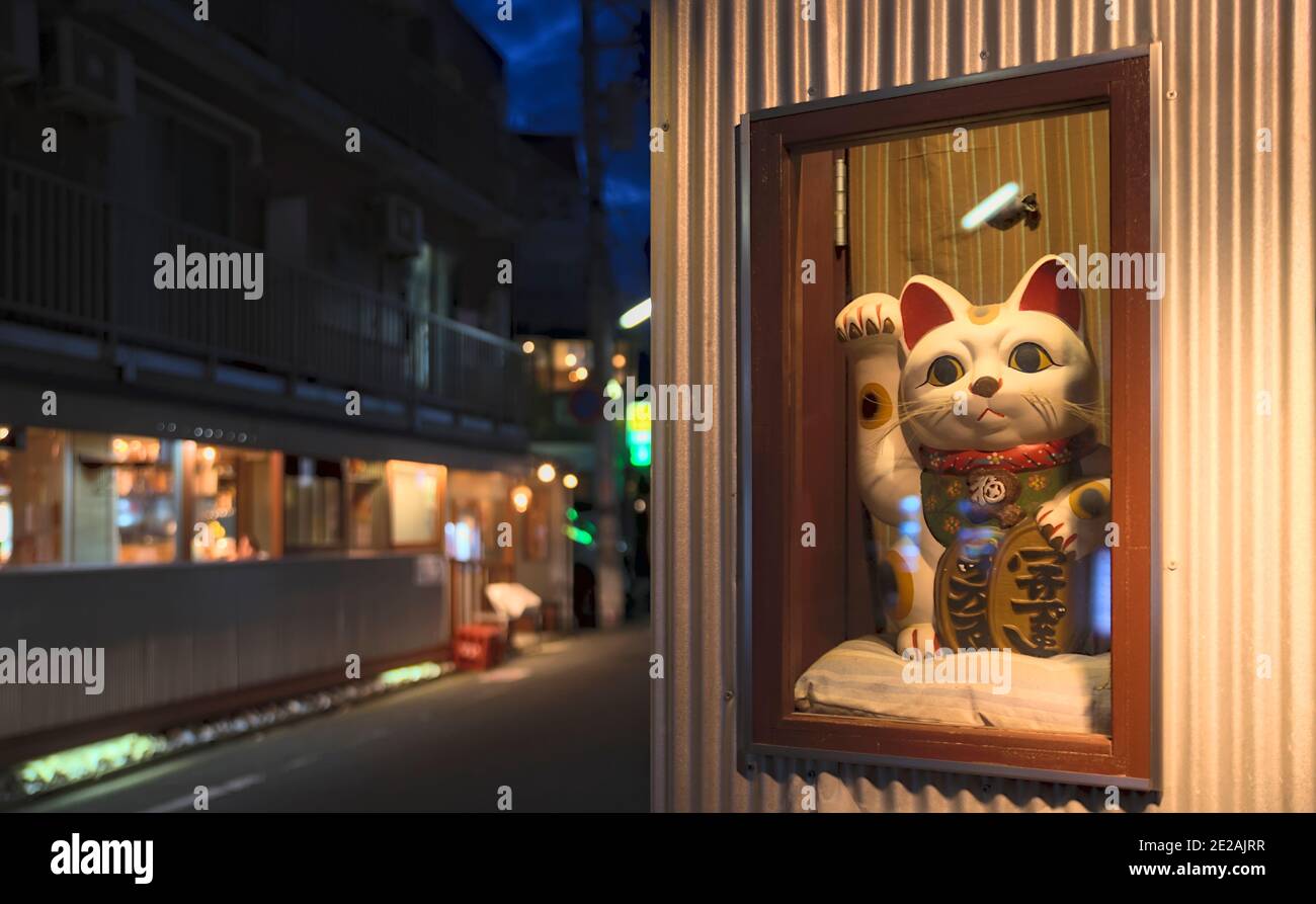 Vue en début de soirée d'un maneki-neko, symbole japonais de bonne fortune, dans une vitrine à l'entrée principale d'un magasin Banque D'Images