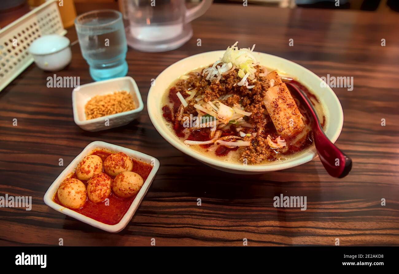 Un bol de nouilles tantanmen avec des côtés d'ail frit morceaux et œufs de caille bouillis marinés épicés sur un bois table dans un restaurant Banque D'Images