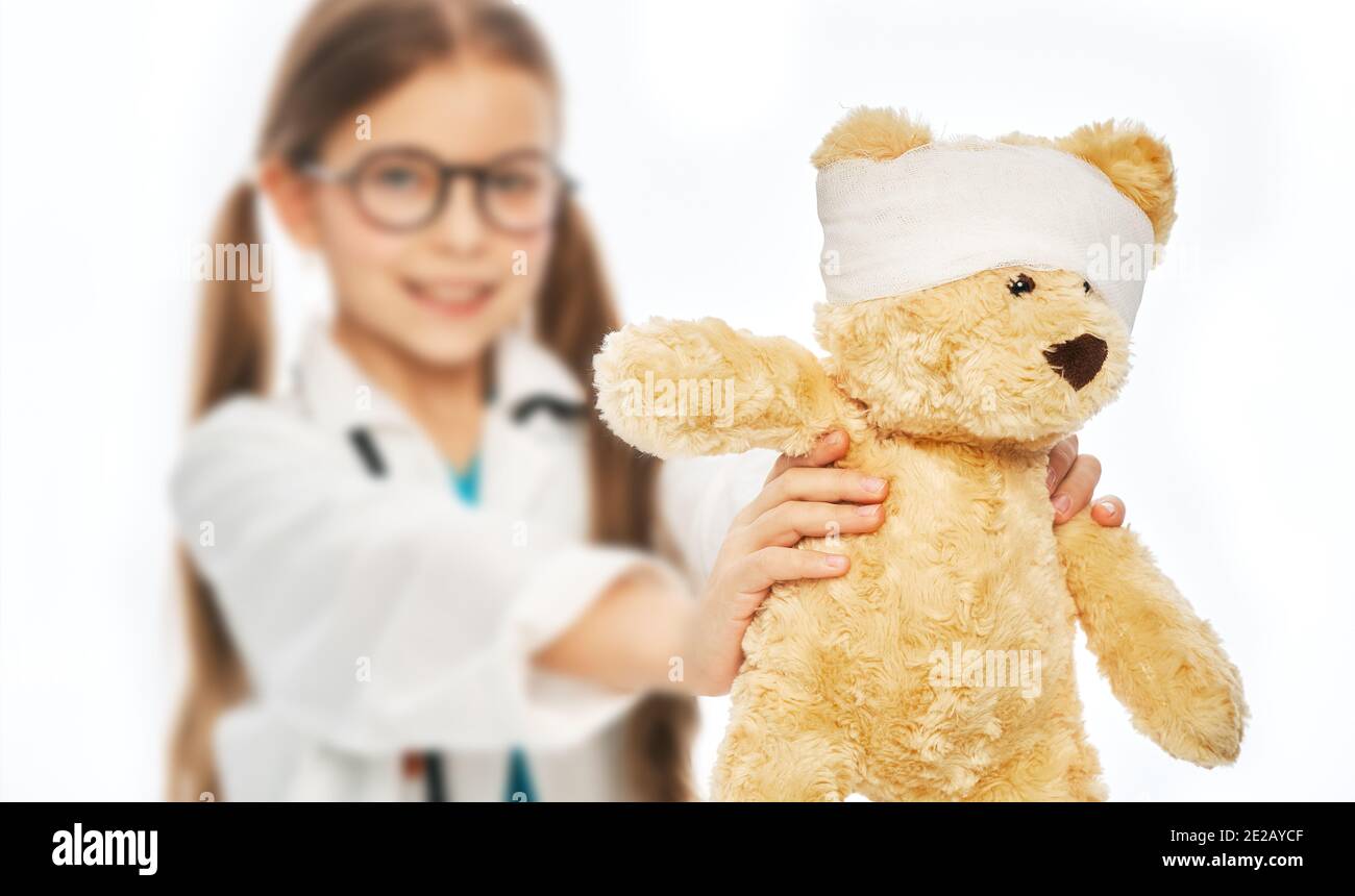 Petite fille portant un manteau médical tenant son ours jouet avec une tête bandée. Soins et assistance aux animaux, vétérinaire Banque D'Images
