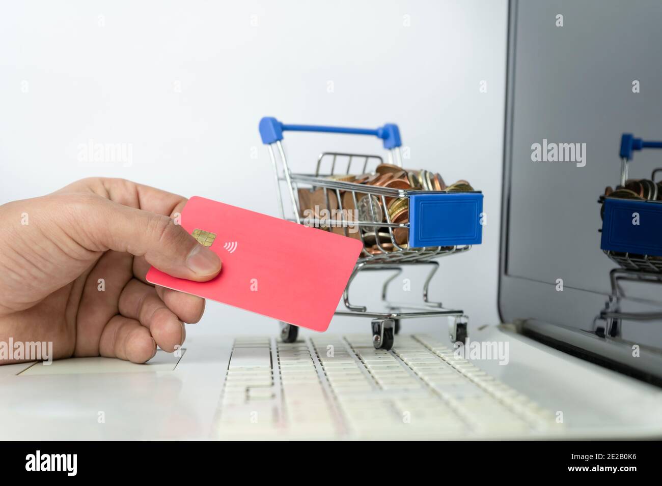 Homme tenant la banque carte de crédit achats en ligne en utilisant ordinateur portable avec supermarché chariot de shopping plein de pièces de monnaie sur blanc Background.E-commerce on Banque D'Images