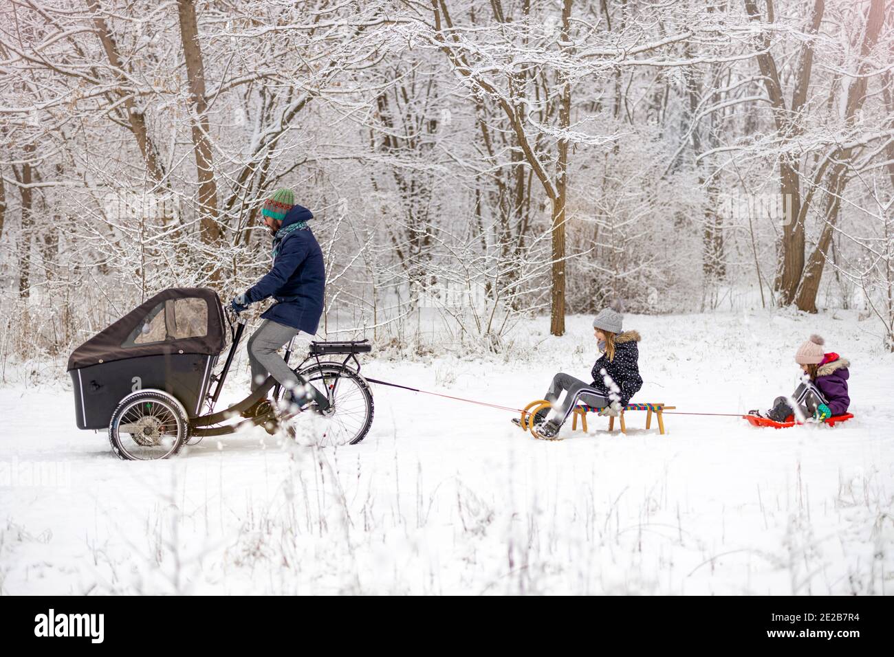 Un homme sur un vélo cargo transporte les enfants sur un traîneau en hiver Banque D'Images