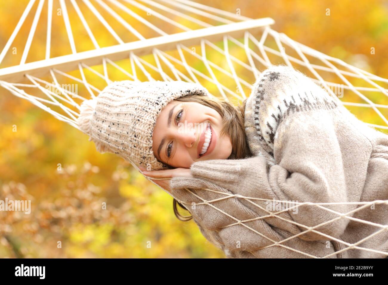 Une femme heureuse avec un sourire parfait reposant sur un hamac regardant caméra en automne dans une forêt Banque D'Images