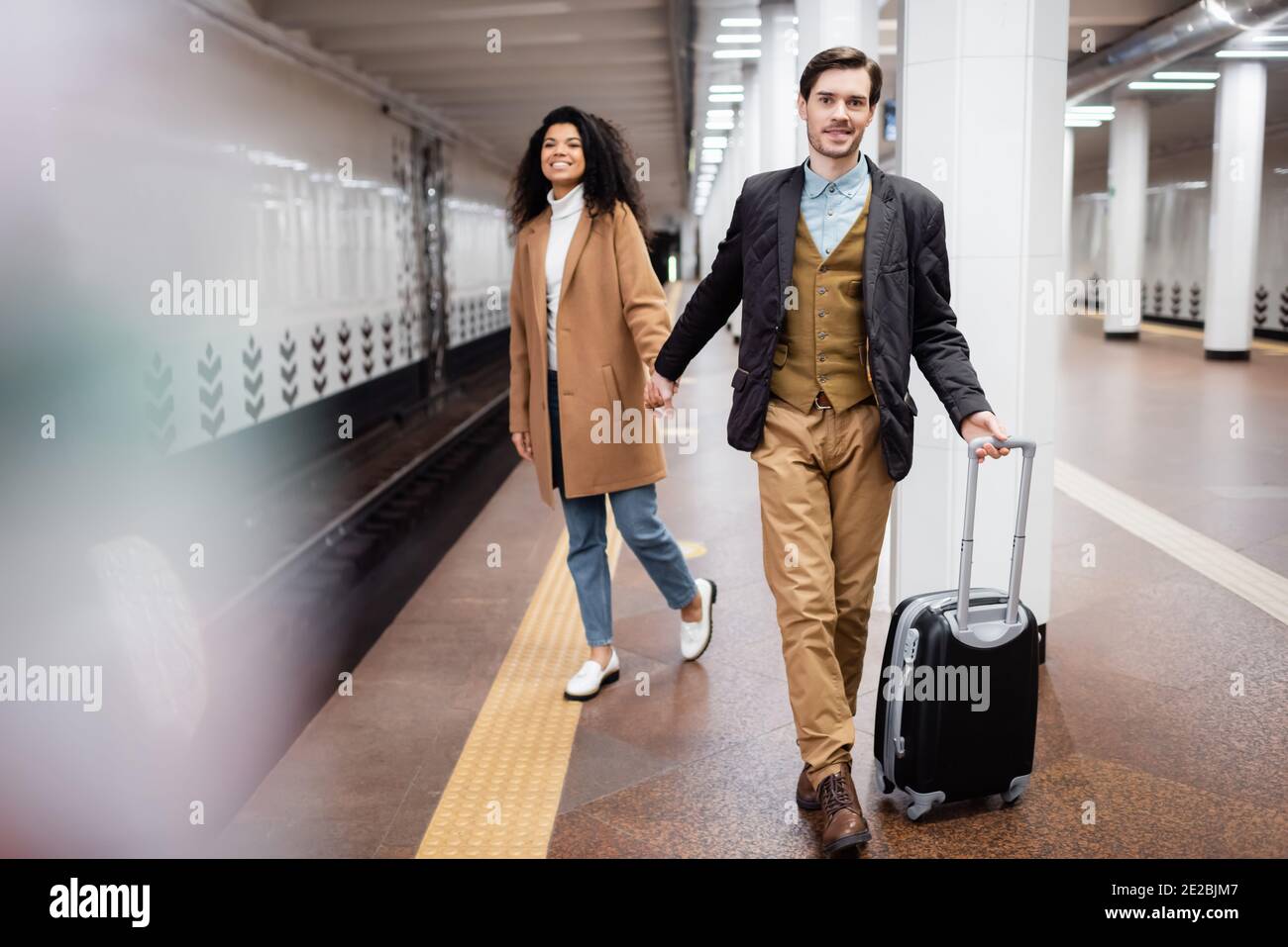 couple interracial tenant les mains dans le métro tout en marchant avec les bagages sur un arrière-plan flou Banque D'Images