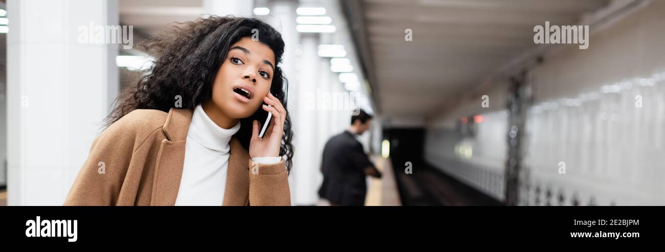 surprise afro-américaine femme parlant sur smartphone et regardant loin dans le métro sur fond flou, bannière Banque D'Images