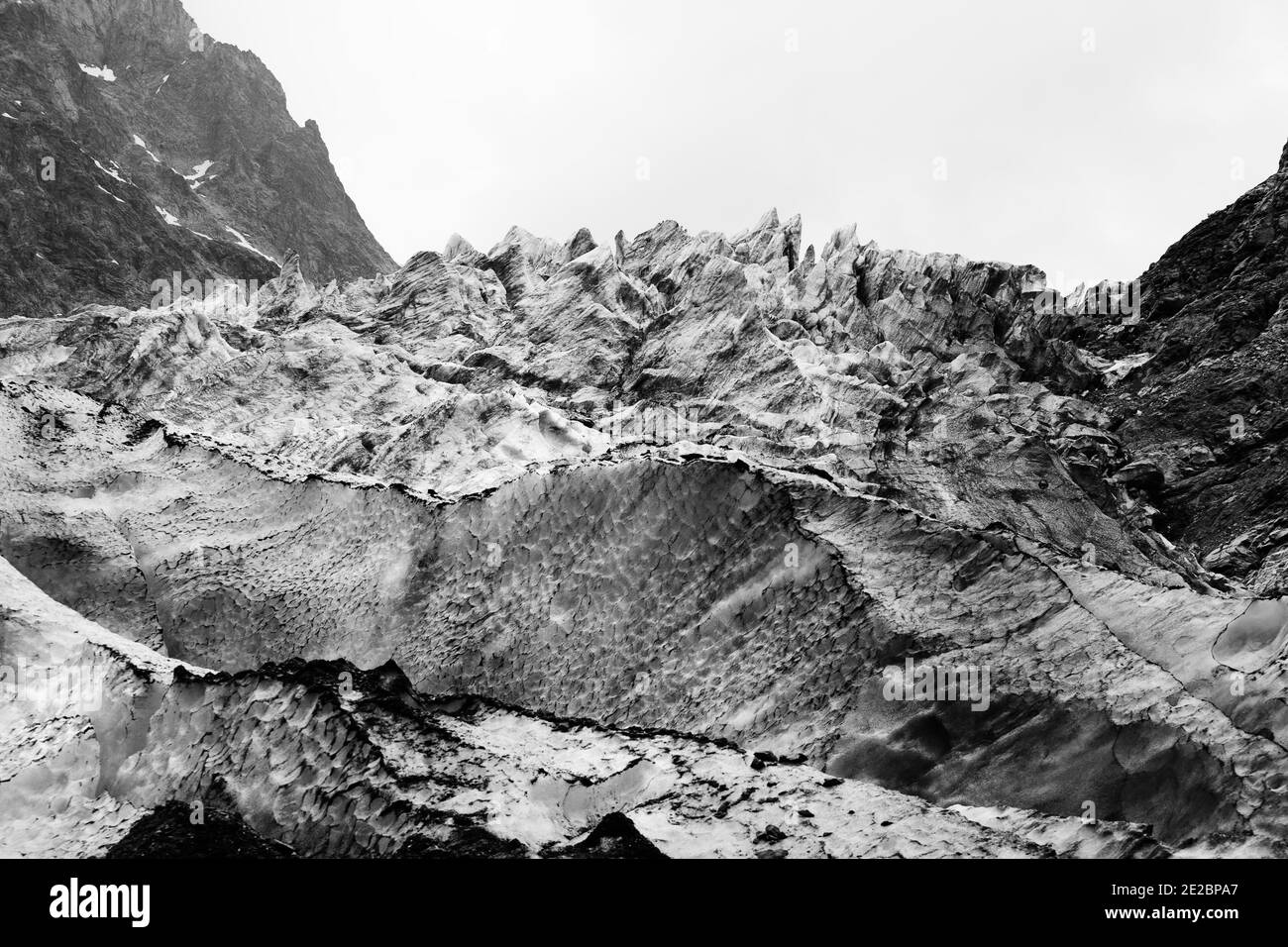 Glacier avec des crevasses profondes couvertes de neige et de terre dans les hautes montagnes rocheuses le jour gris. Montagnes du Caucase. Géorgie, région de Svanetia. Emplacement distant Banque D'Images