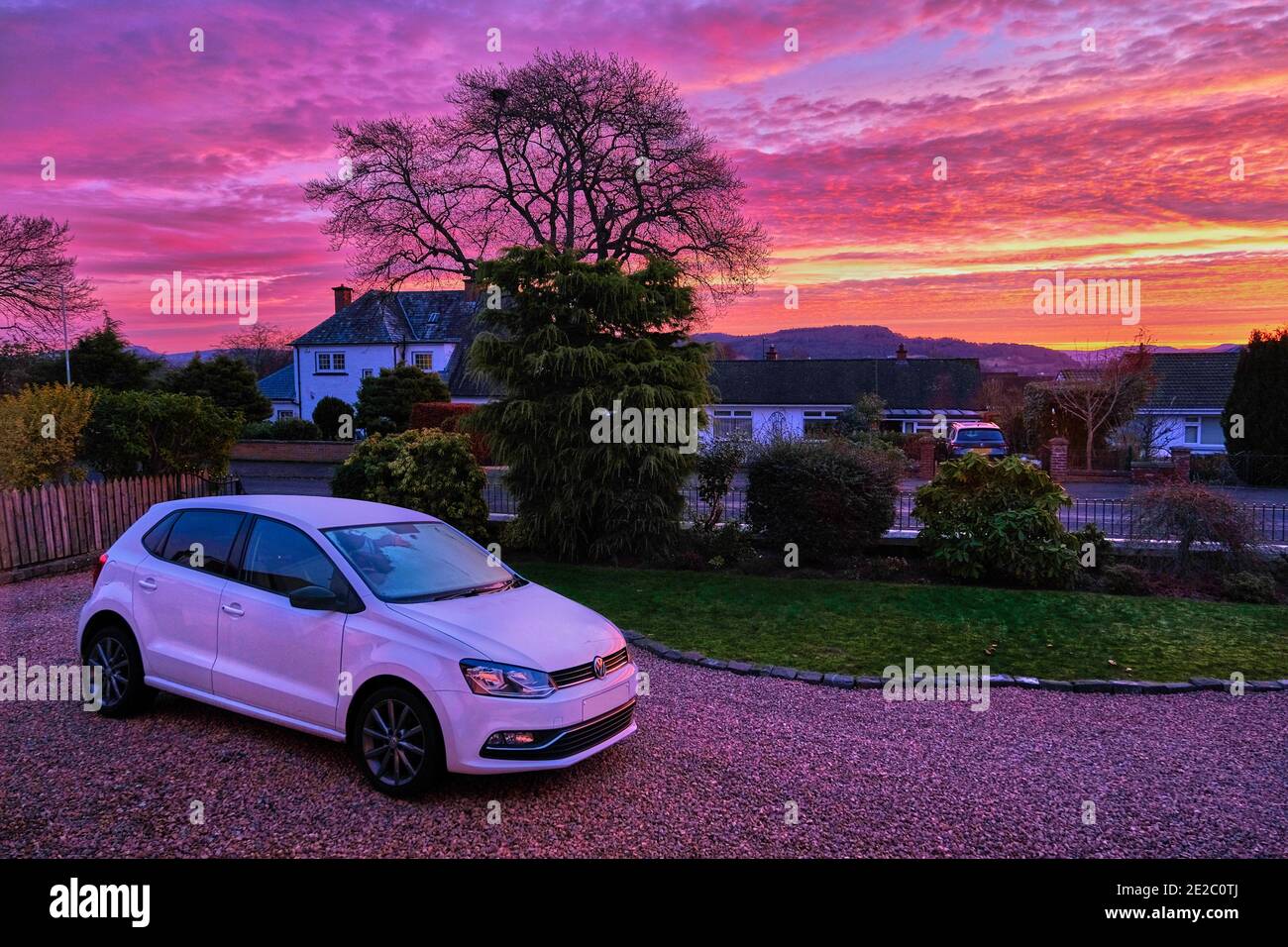 Un lever de soleil enflammé et un VW Polo blanc garés sur une route de gravier. Banque D'Images