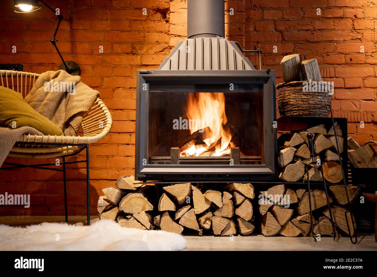 Cheminée confortable avec bois de chauffage dans la maison de style loft avec arrière-plan de mur de briques, feu de cheminée dans la cheminée, agrément de la maison en hiver Banque D'Images
