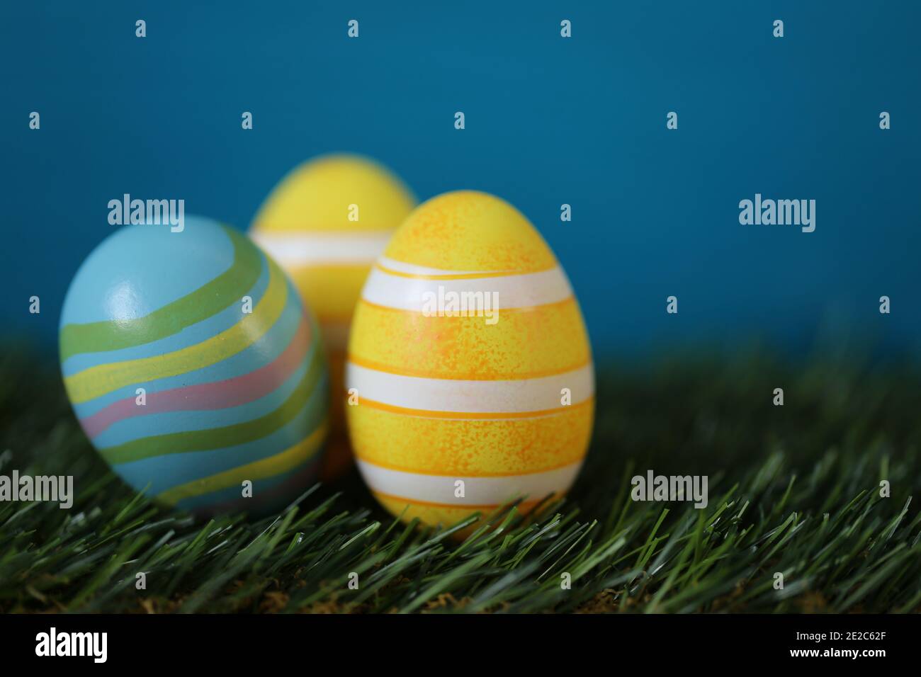 Vacances de Pâques. Œufs rayés jaunes de Pâques dans l'herbe verte sur un fond bleu turquoise vif.Printemps fond festif de pâques.symbole de Pâques. Copie Banque D'Images