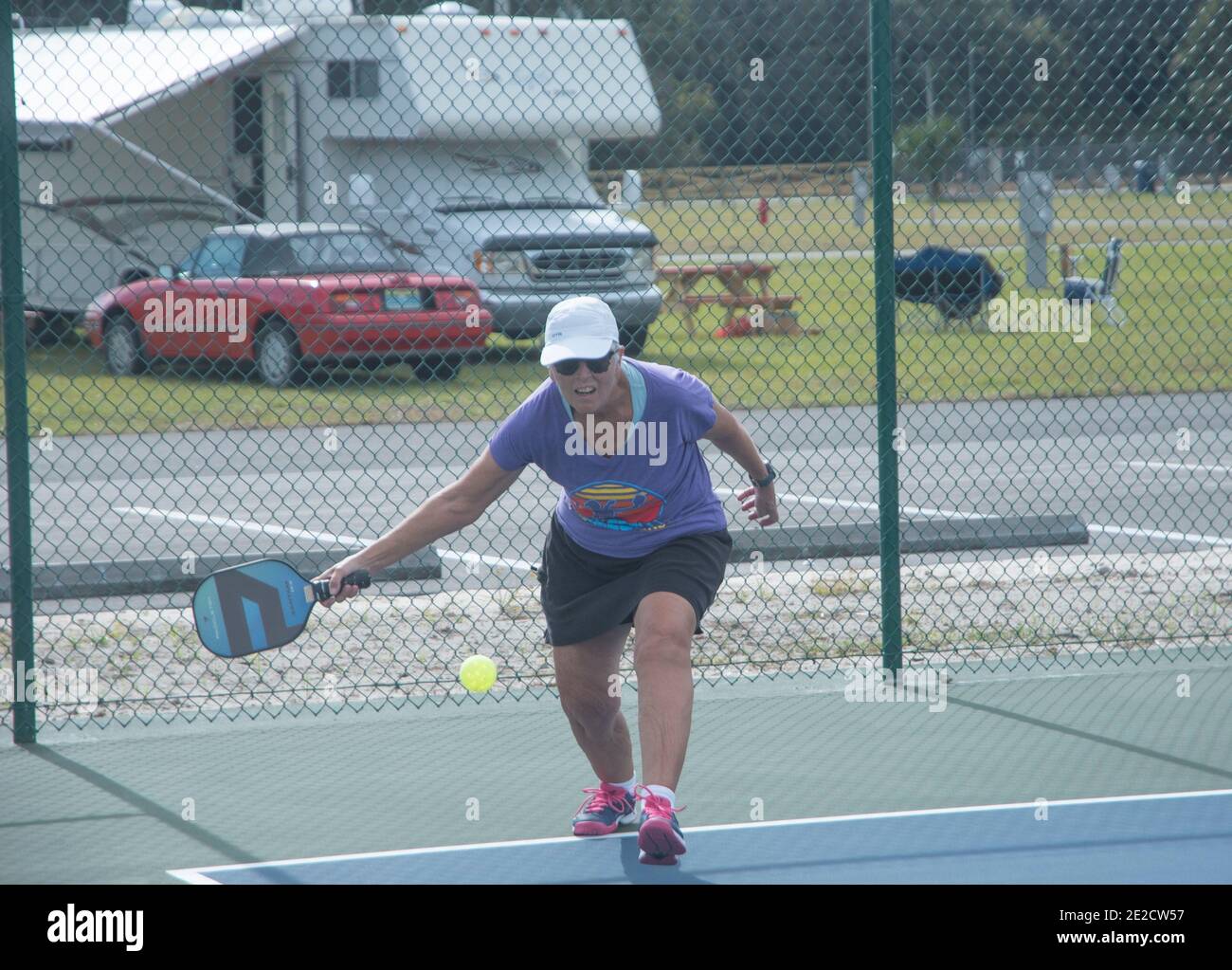 Avec des campeurs et des véhicules de camping à l'arrière-plan, une femme frappe un pickleball. Pickleball est devenu l'un des sports à la croissance la plus rapide. Banque D'Images