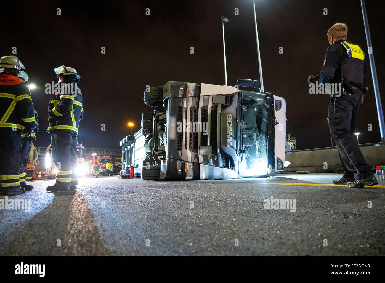 Hambourg, Allemagne. 13 janvier 2021. Des pompiers et un policier se tiennent à côté du camion articulé renversé sur l'autoroute 7. Un camion a été renversé mercredi soir devant le tunnel Elbe de Hambourg. Le conducteur a été légèrement blessé, a déclaré un porte-parole de la police. Credit: Jonas Walzberg/dpa - ATTENTION: (Plaques d'immatriculation de camion ont été pixelated pour des raisons de confidentialité)/dpa/Alay Live News Banque D'Images