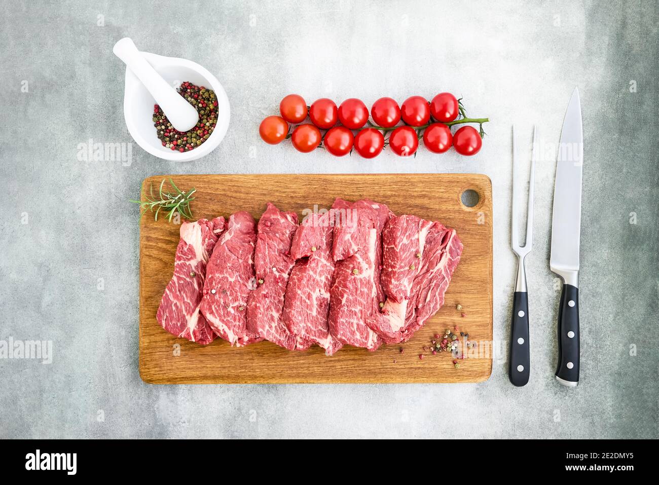 Steaks de bœuf frais crus au poivre et aux tomates sur planche à découper en bois. Espace de copie, vue de dessus. Pose à plat Banque D'Images