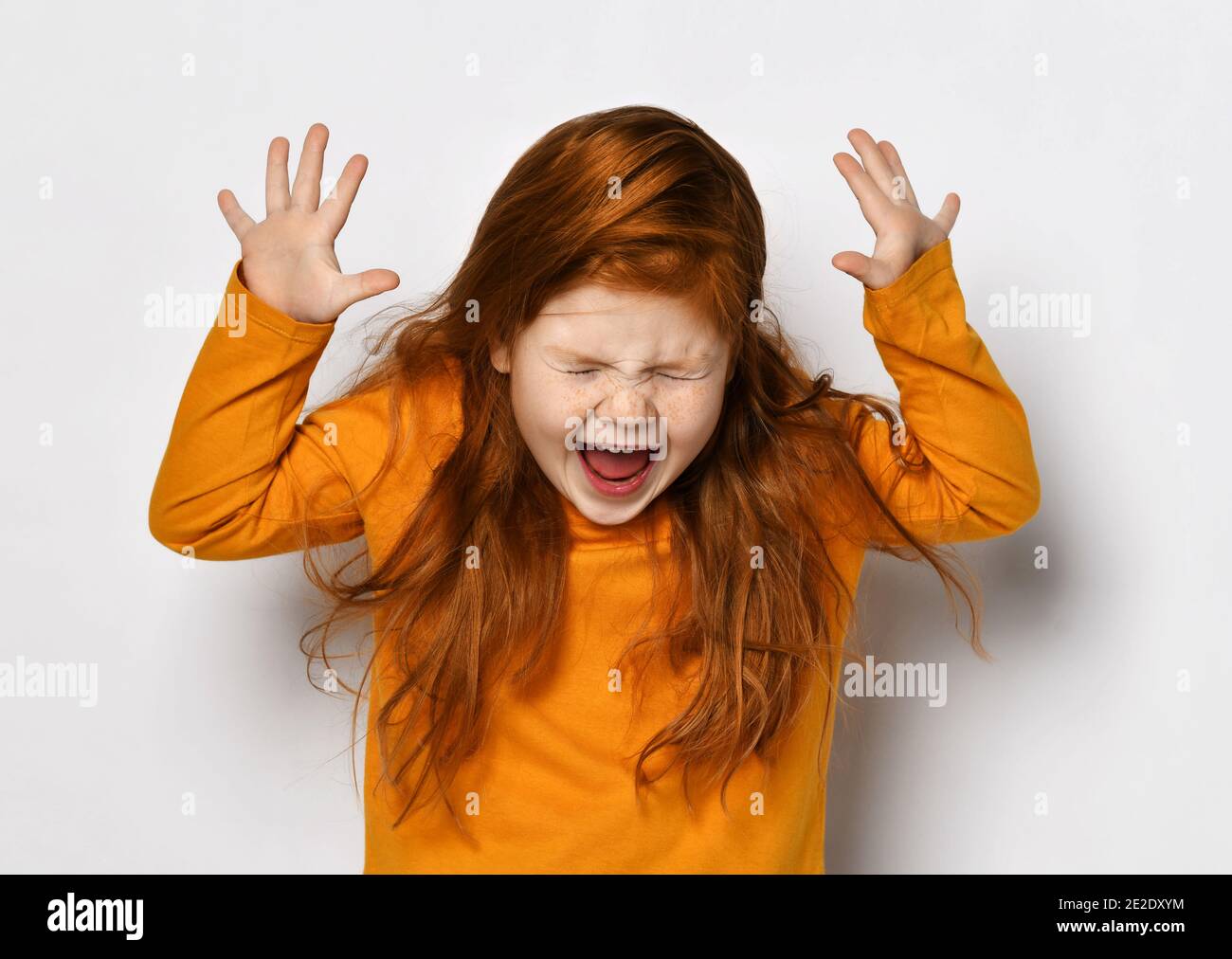 Joyeuse petite fille aux cheveux rouges avec des taches de rousseur à manches longues jaunes se sentir fou et excité avec les yeux fermés et la bouche ouverte Banque D'Images