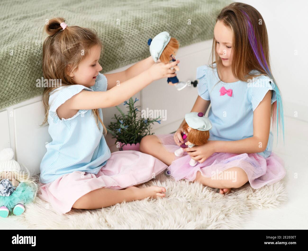 Deux filles actives et heureuses sœurs en robes bleues jouent avec leurs poupées se rencontrent sur tapis doux de tapis à accueil Banque D'Images