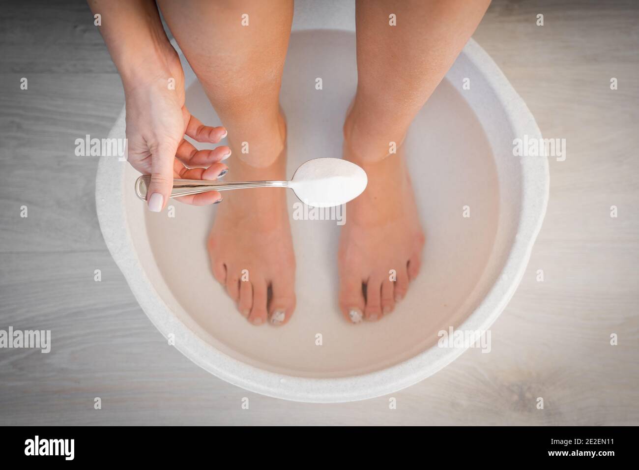 Femme a mis une cuillère de bicarbonate de soude dans le bain avec de l'eau chaude pour ses pieds. Bain maison pour les pieds secs. Banque D'Images