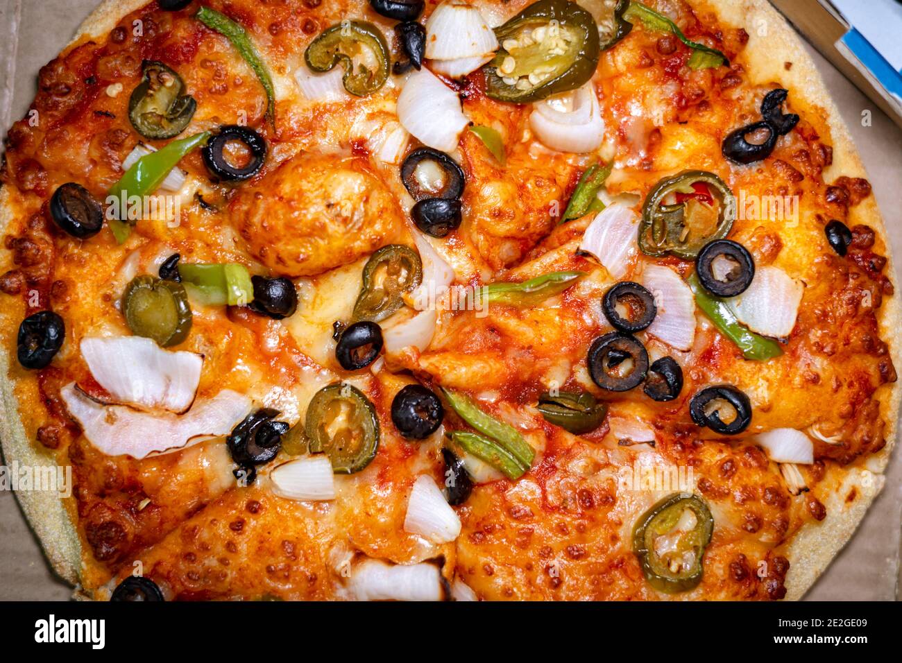 Vue de dessus d'une pizza végétarienne à la cheesy, surmontée d'olives noires, de poivrons verts, d'oignons et de jalapeño dans une boîte à emporter Banque D'Images