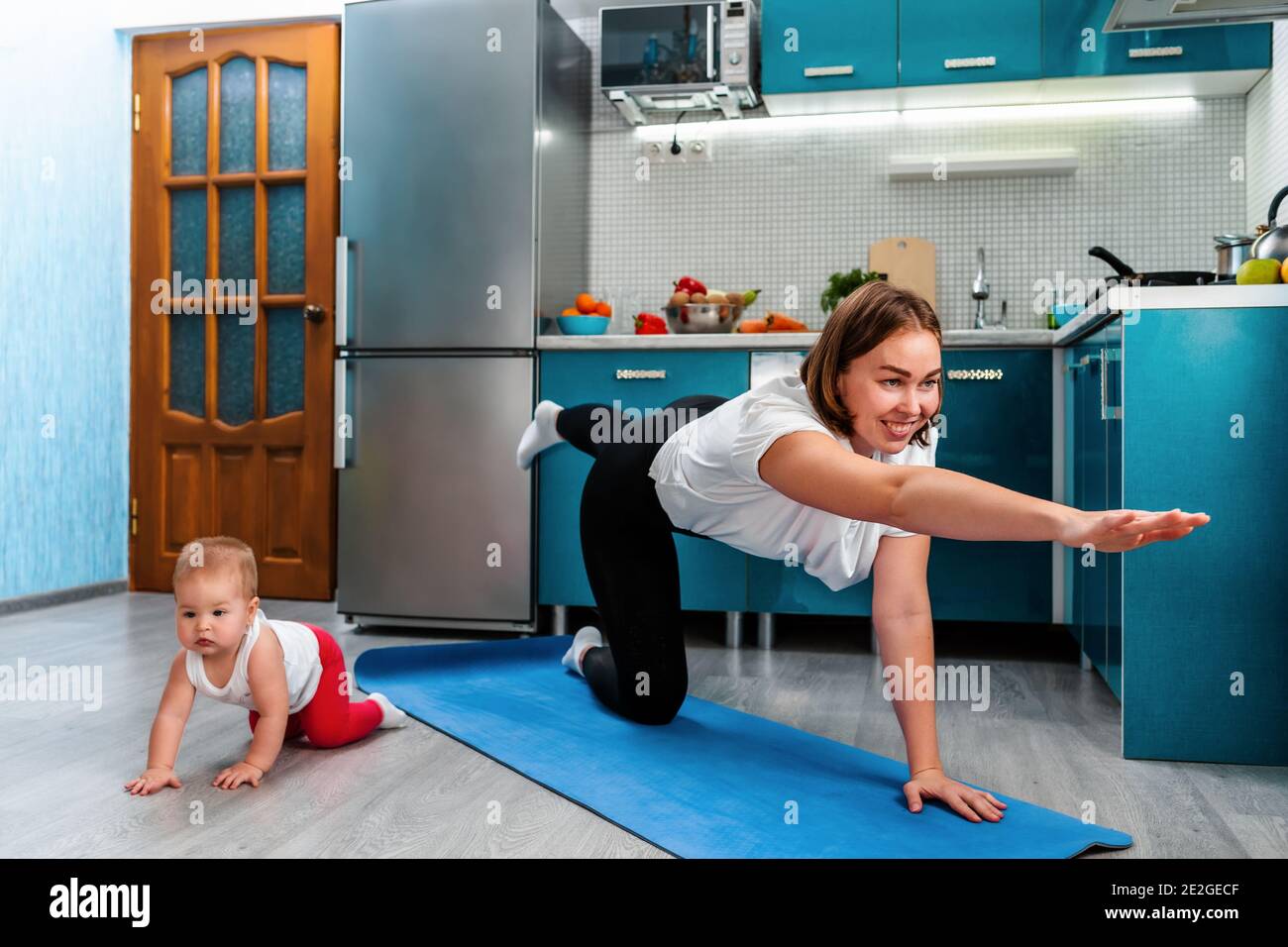 Une Jeune Mere Souriante Fait Un Asana De Yoga Sur Un Tapis Tandis Que Son Bebe Rampe A Cote D Elle Sur Le Sol Sports Et Yoga A La Maison Avec Les Enfants