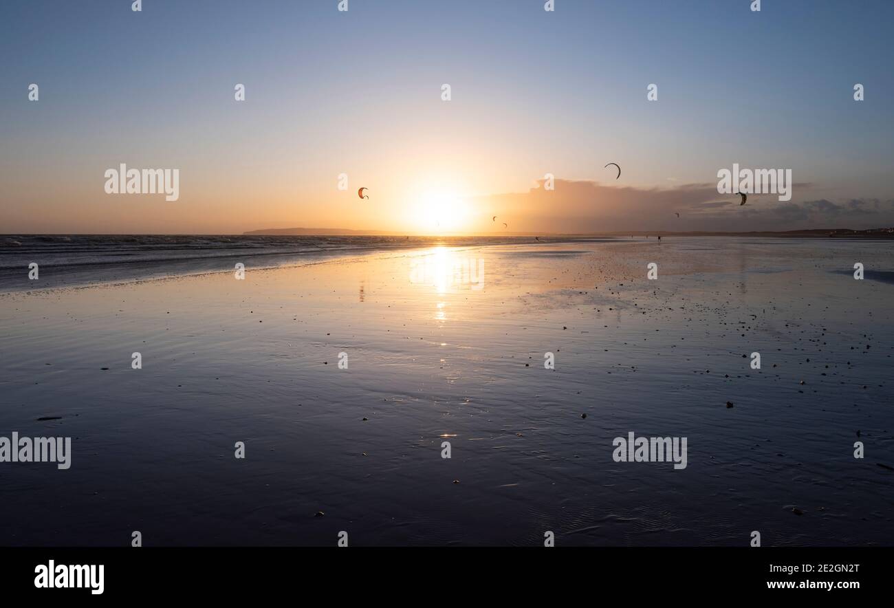 Cerfs-volants et surfeurs sur la côte sud à Camber Sands, East Sussex au coucher du soleil. Banque D'Images