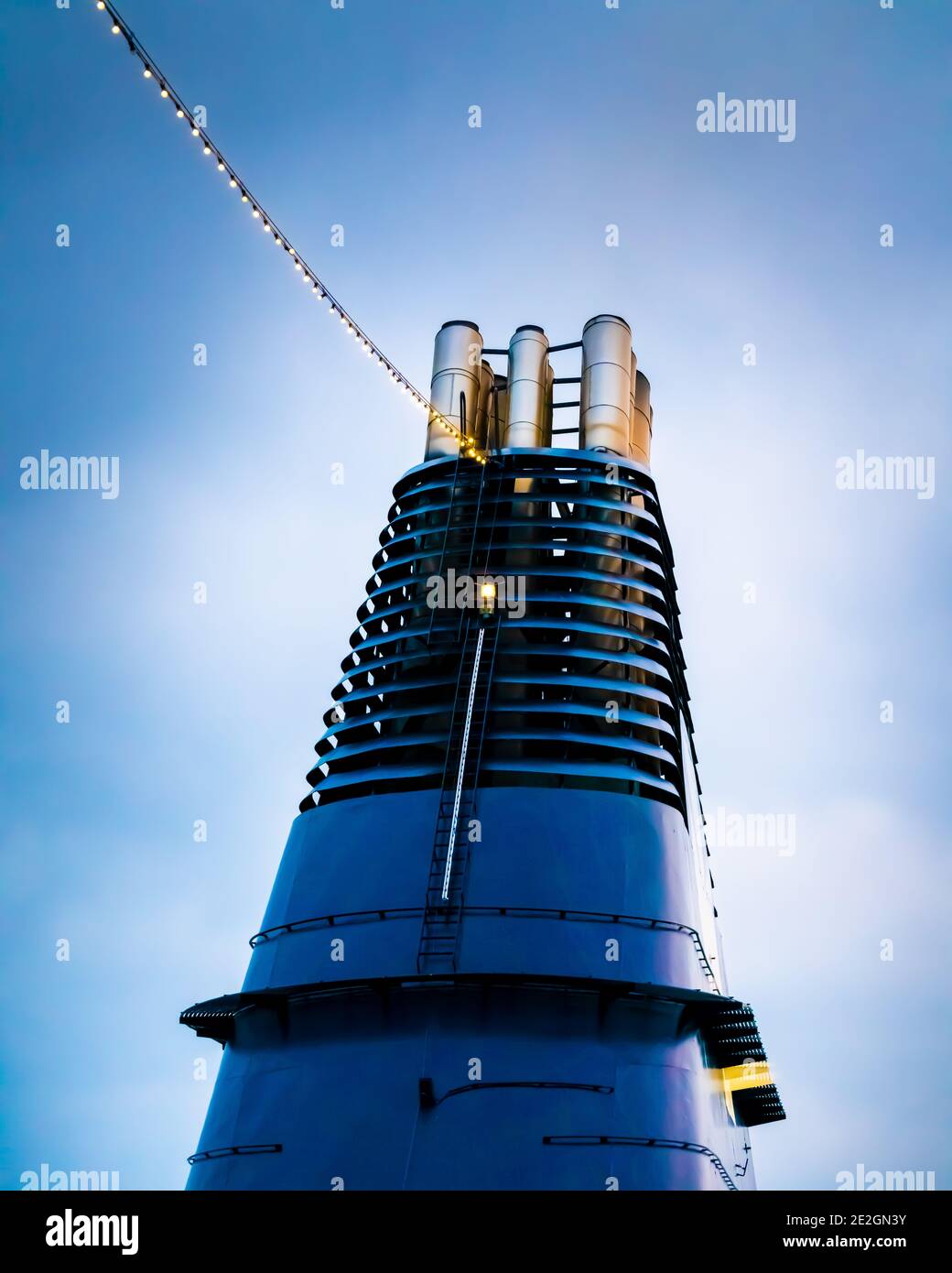 Smokestack sur un grand bateau de croisière avec des chaînes légères et ciel moody. Banque D'Images