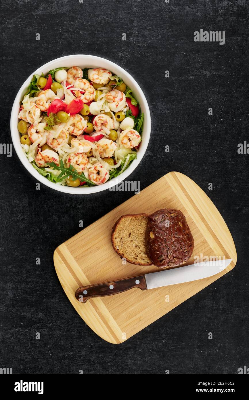 Salade délicieuse avec crevettes, olives, mozzarella, tomates, sauce à l'huile d'olive et petits pains de seigle sur fond sombre, plat Banque D'Images
