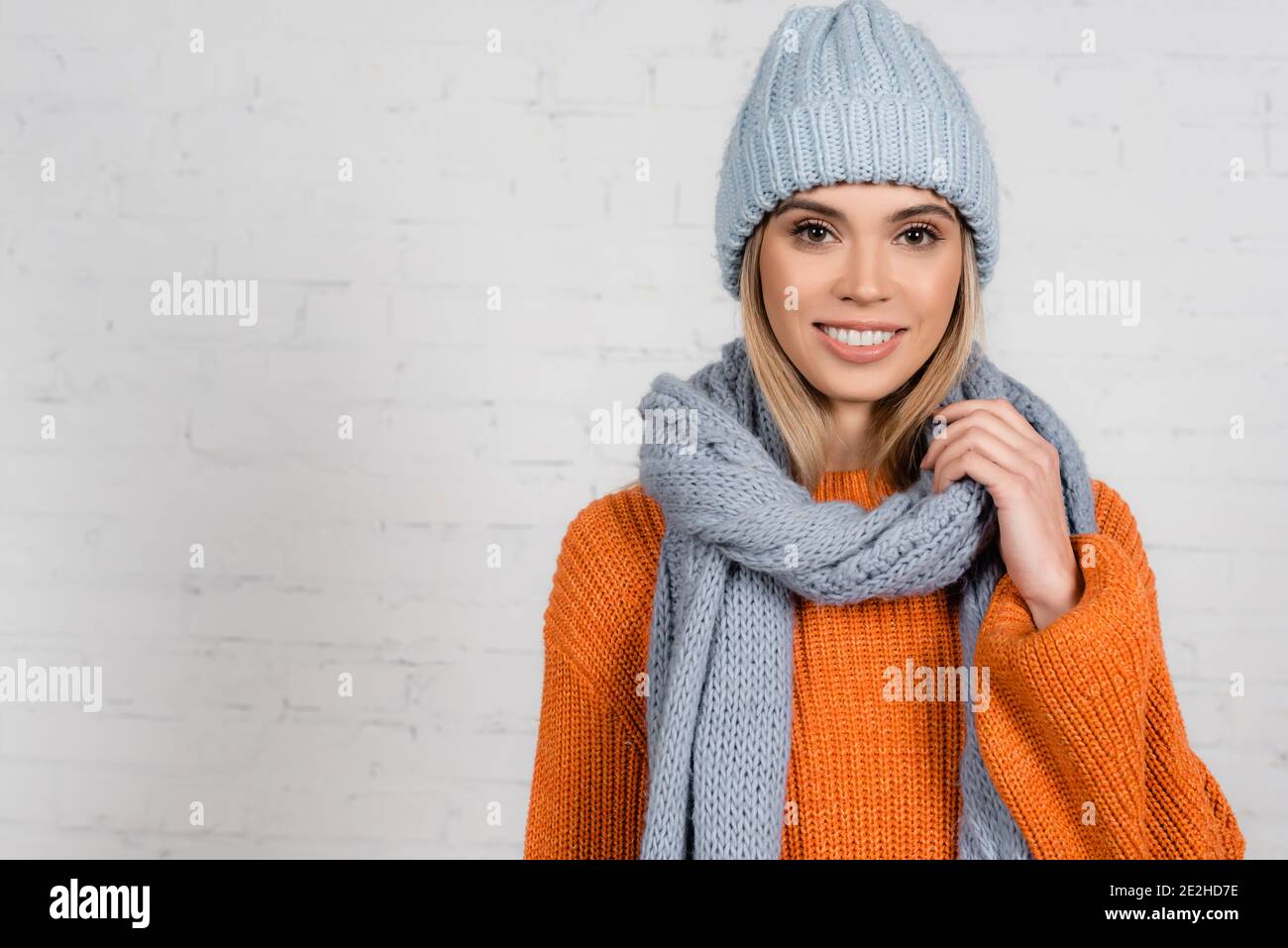 Femme gaie en foulard et chandail chaud près de la brique blanche mur Banque D'Images