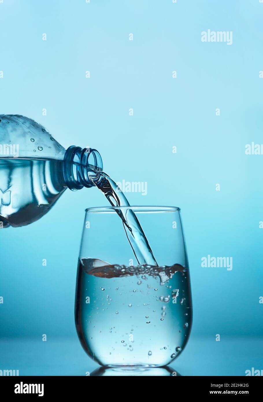 De l'eau fraîche coule de la bouteille en plastique dans un verre sur fond  bleu avec espace de copie, orientation verticale Photo Stock - Alamy