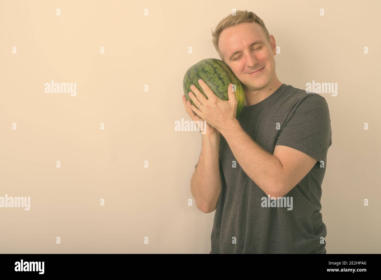 Studio shot of young handsome man holding watermelon que bébé avec les yeux fermés contre fond blanc Banque D'Images