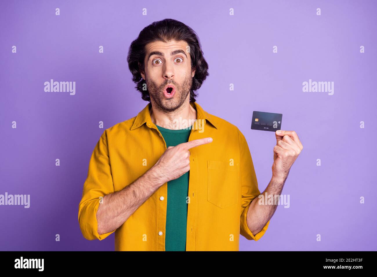 Photo portrait d'un homme choqué tenant une carte de crédit en un doigt pointant isolé sur un arrière-plan violet vif Banque D'Images