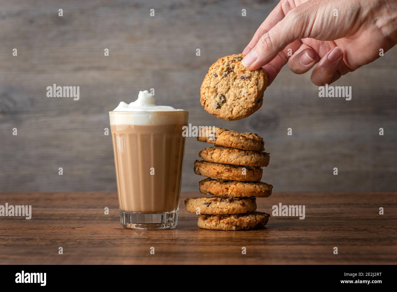 Latte à café dans un verre avec une main qui se prépare un cookie sur une table en bois Banque D'Images