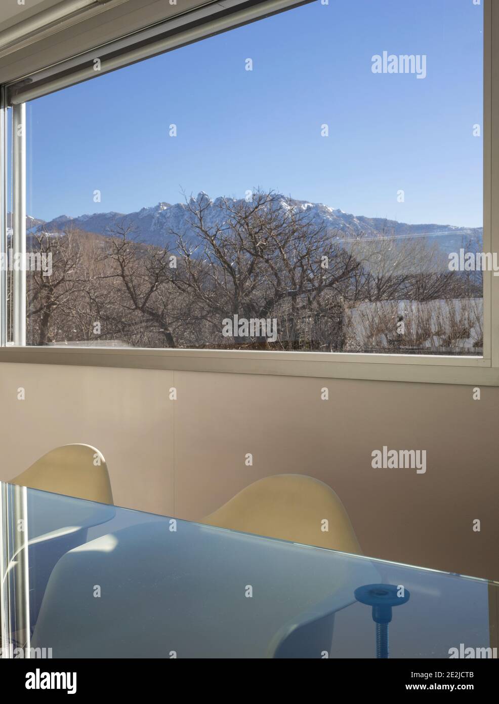 Détail d'une grande fenêtre donnant sur la nature et une table en verre avec deux chaises à l'avant. Banque D'Images