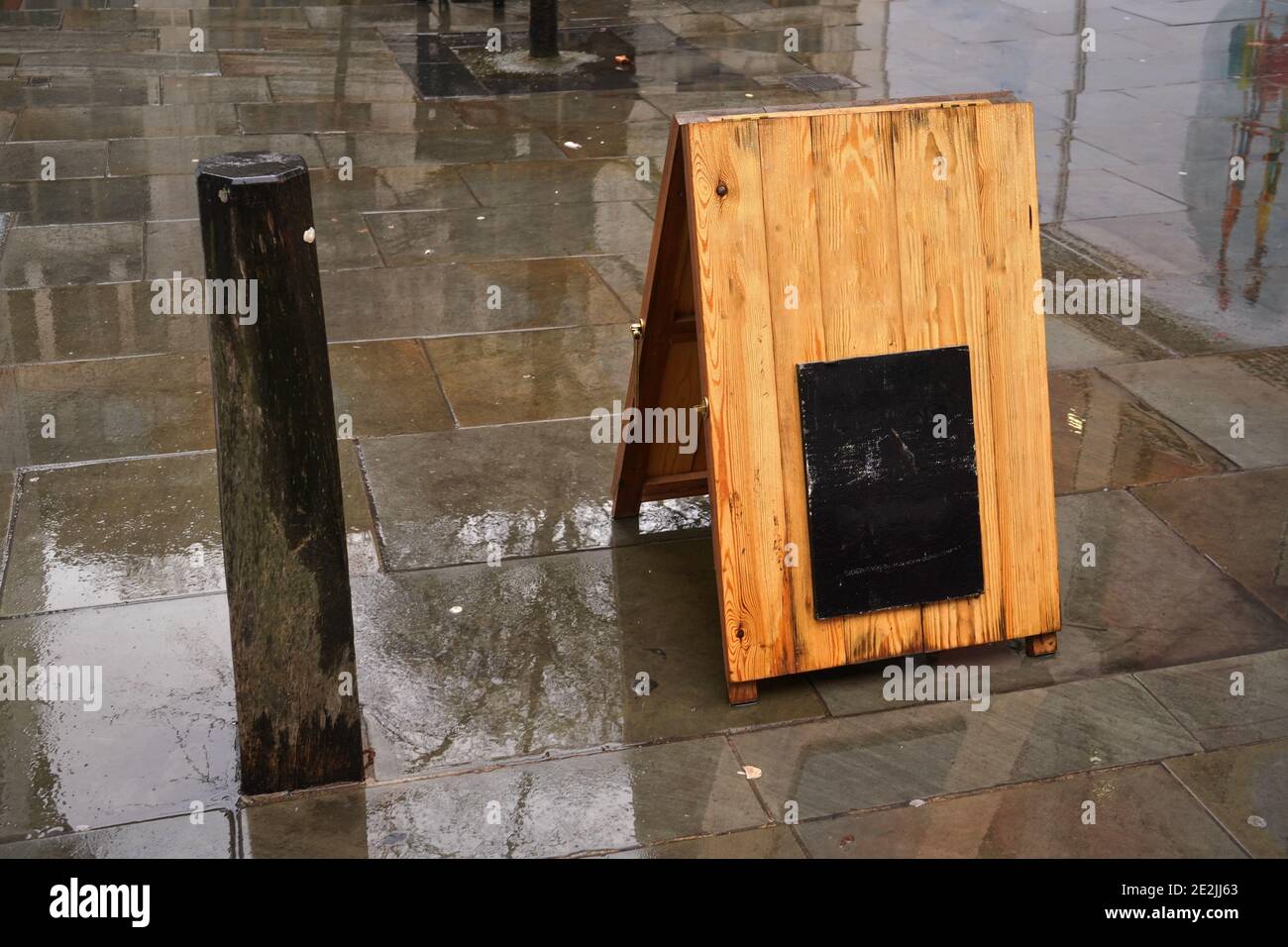 Support en bois avec petit tableau noir vide (espace pour votre texte) dans une rue mouillée par la pluie Banque D'Images