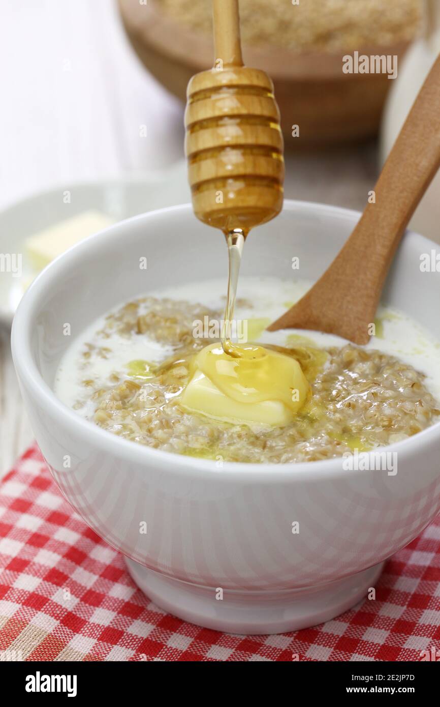 Faire tomber le miel par un balancier en bois sur le porridge écossais avec du lait et du beurre. Banque D'Images