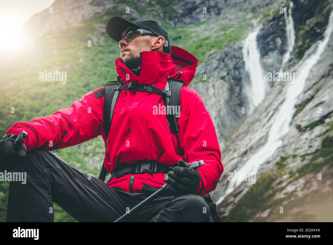 Loisirs en plein air. Active Caucasien Hiker porter une veste rouge imperméable et des yeux lunettes de sécurité se place à côté des cascades alpines pittoresques. Explorer le Banque D'Images