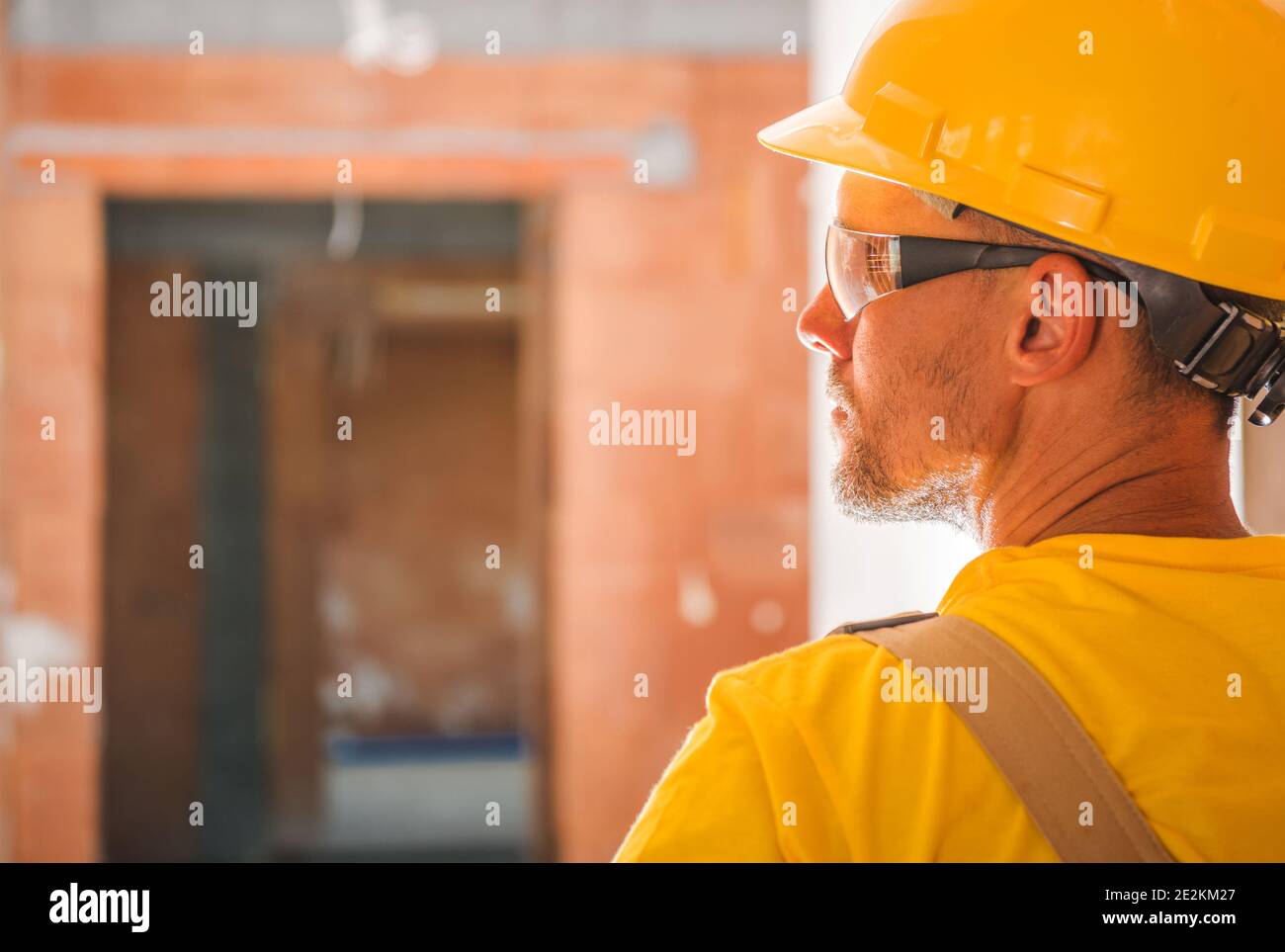 Uniforme jaune et casque dur portant un travailleur de la construction à l'intérieur d'un bâtiment commercial en brique de béton nouvellement construit. Vue de face arrière. Profess de construction Banque D'Images