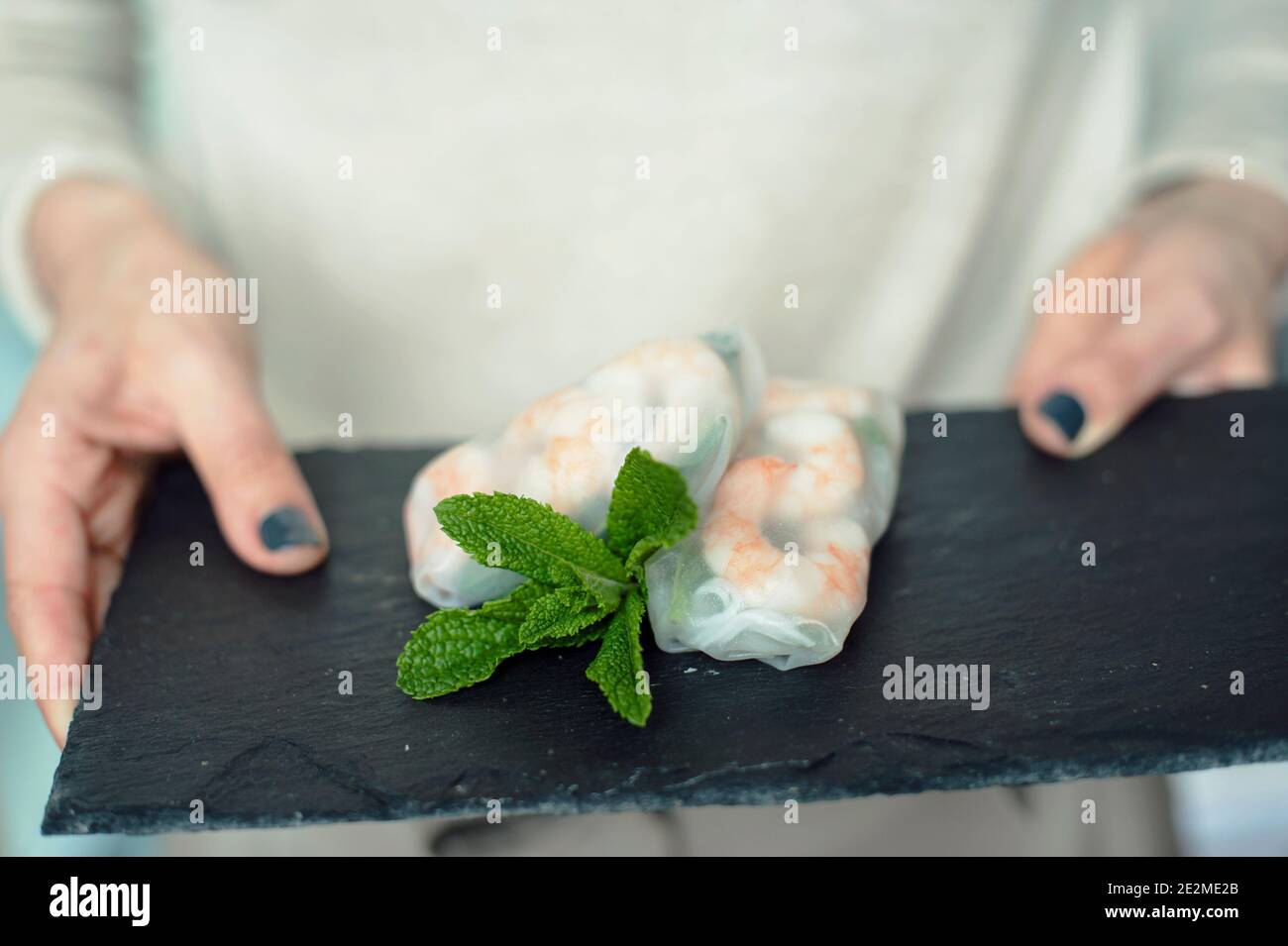 Femme mains tenant un plateau d'ardoise de pierre noire et des rouleaux d'été vietnamiens faits maison avec des crevettes. En-cas sains et sans gluten Banque D'Images