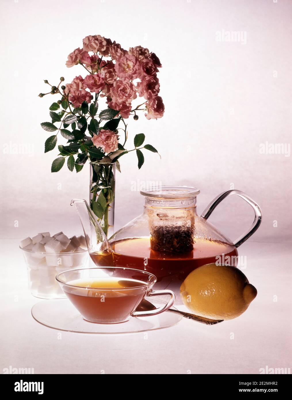 TASSE DE THÉ DES ANNÉES 1980 INFUSER EN VERRE TRANSPARENT THÉIÈRE SUCRE CITRON CUBES ET VASE DE FLEURS DE CARNATION ROSE - KF18511 DAS001 HARS À L'ANCIENNE Banque D'Images