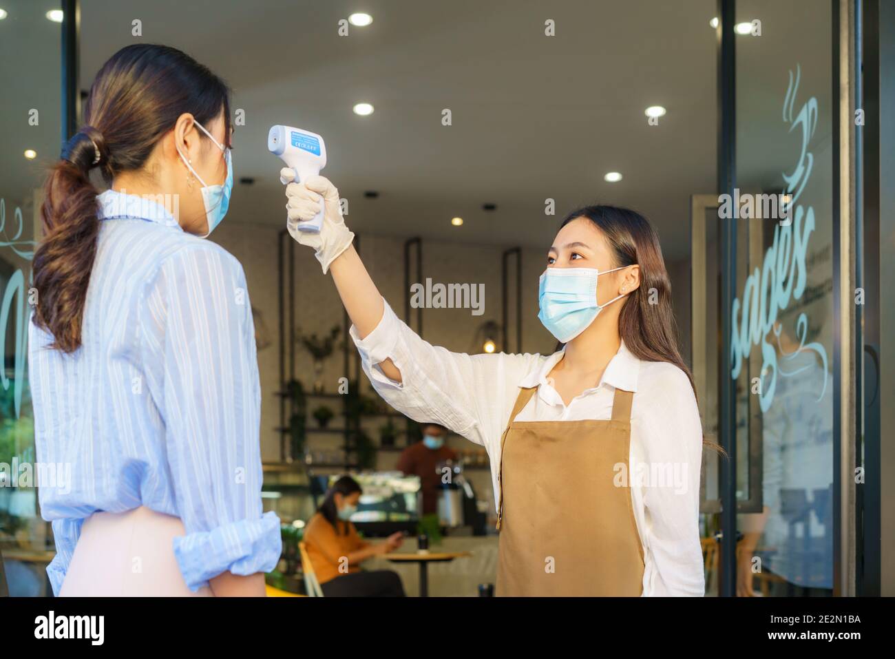 Femme asiatique employé de café prendre la température femme asiatique avec le visage masque avant d'aller au restaurant ou au café pour nouveau coronavirus cov de style de vie normal Banque D'Images