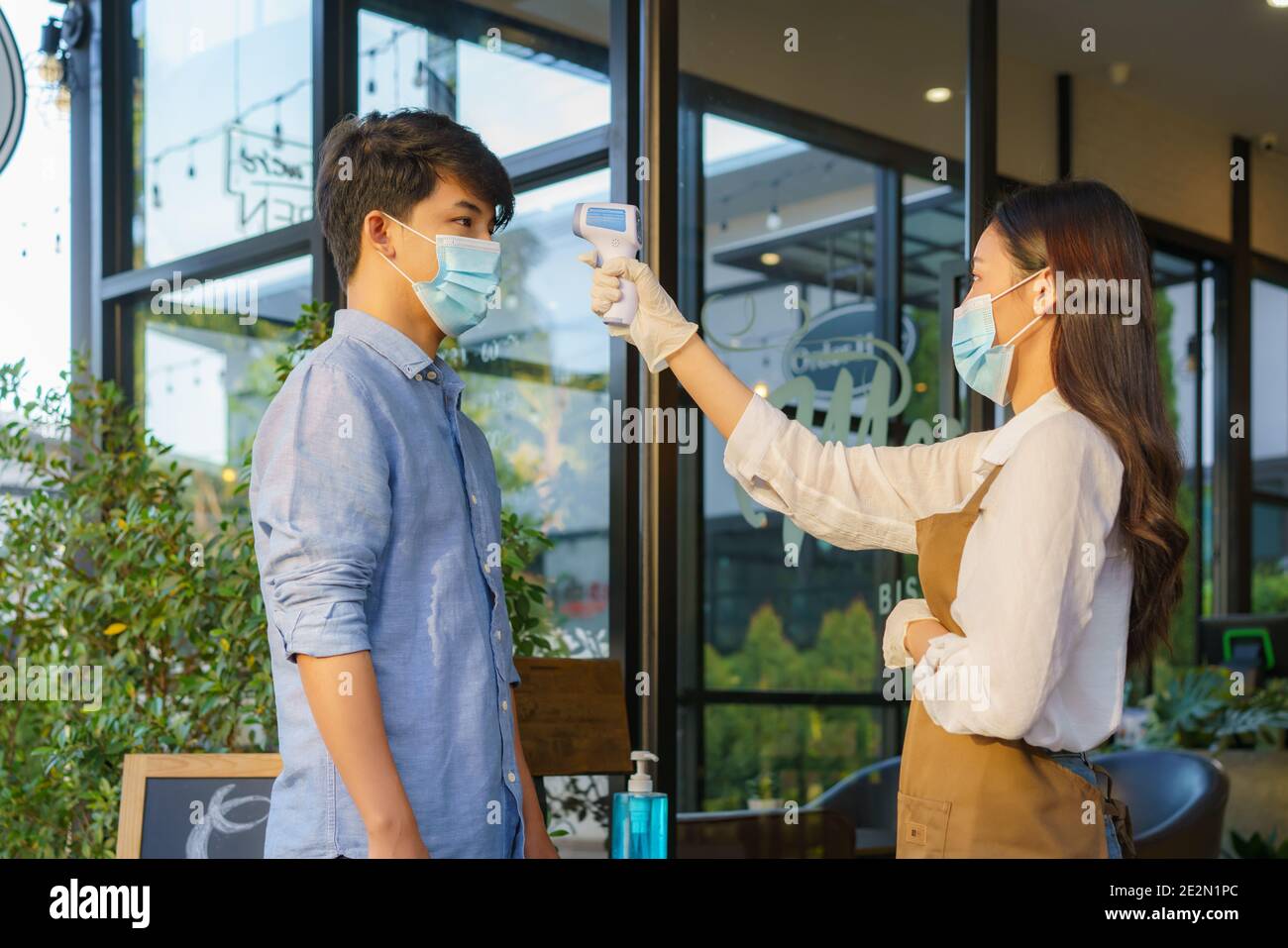 Femme asiatique employé de café après prendre la température homme asiatique avec masque avant d'aller au restaurant ou au café pour nouveau coronavirus de style de vie normal Banque D'Images