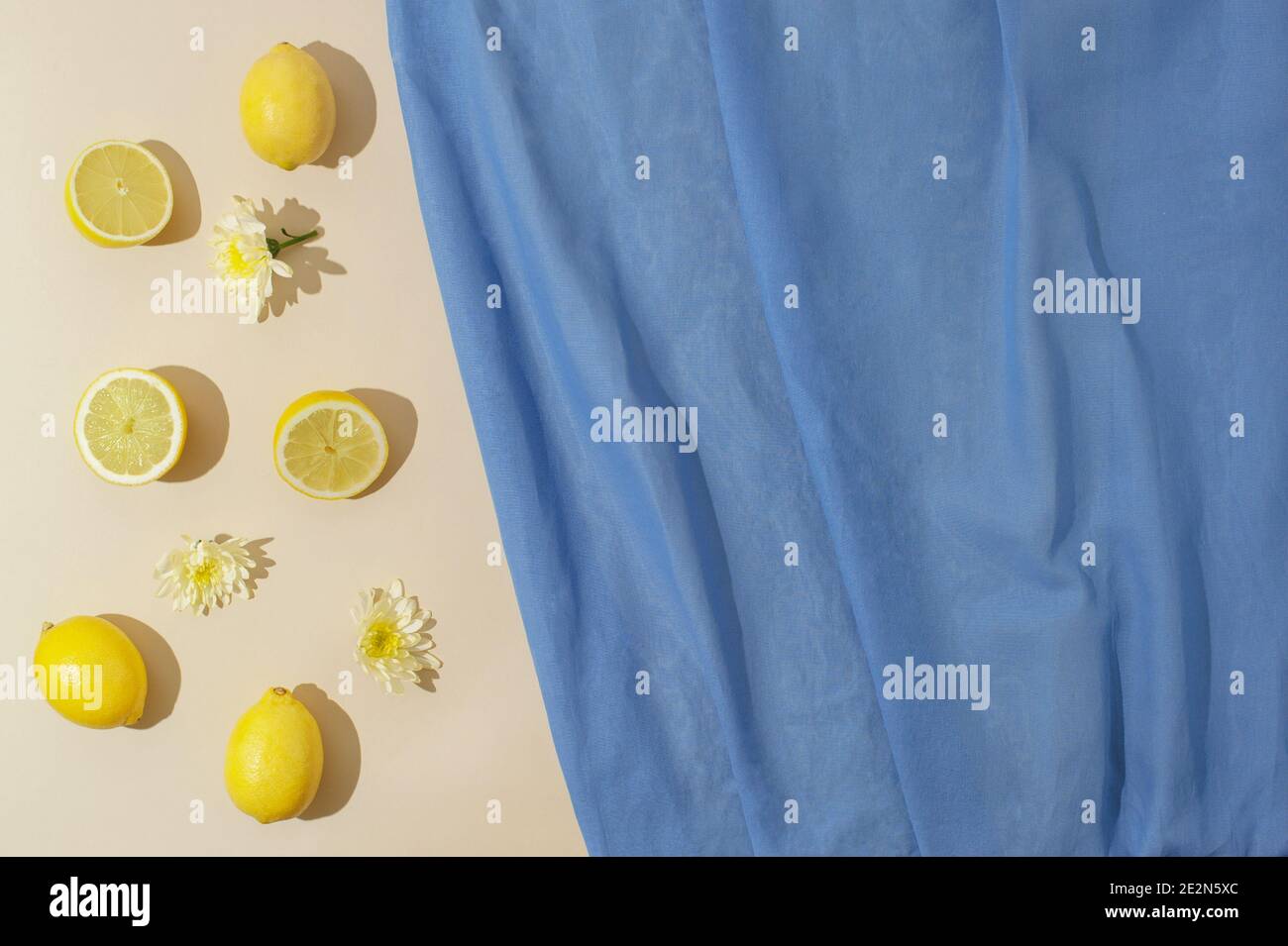 Scène estivale avec citrons, fleurs jaunes et linge bleu sur fond de sable pastel. Pose à plat avec peu de lumière du soleil. Banque D'Images